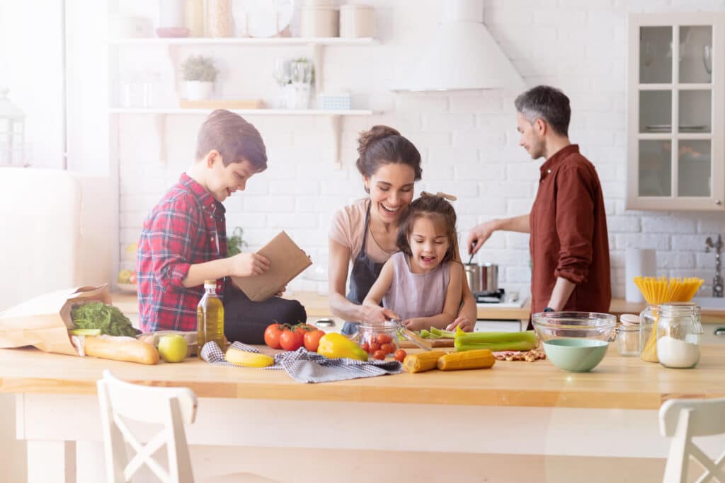 Why Kylie Kelce refuses to give ‘sibling gifts’ and 10 alternatives for parents who agree | "I am vehemently against the idea of other kids getting birthday presents on a child's birthday.” Pregnancy News family preparing dinner in the kitchen