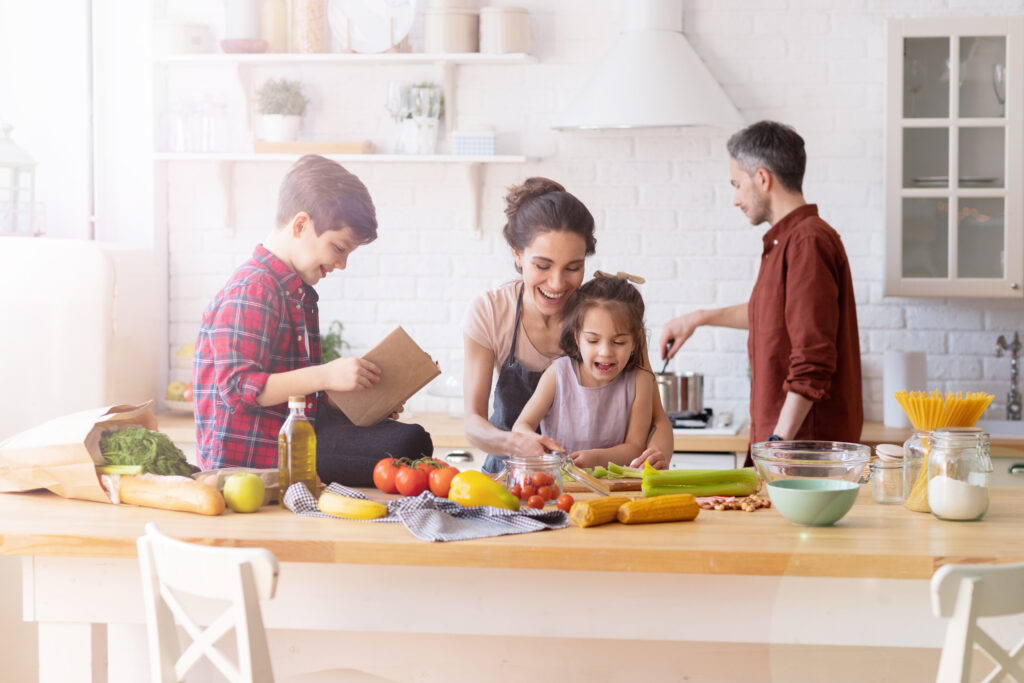 Why Kylie Kelce refuses to give ‘sibling gifts’ and 10 alternatives for parents who agree | "I am vehemently against the idea of other kids getting birthday presents on a child's birthday.” Pregnancy News family preparing dinner in the kitchen