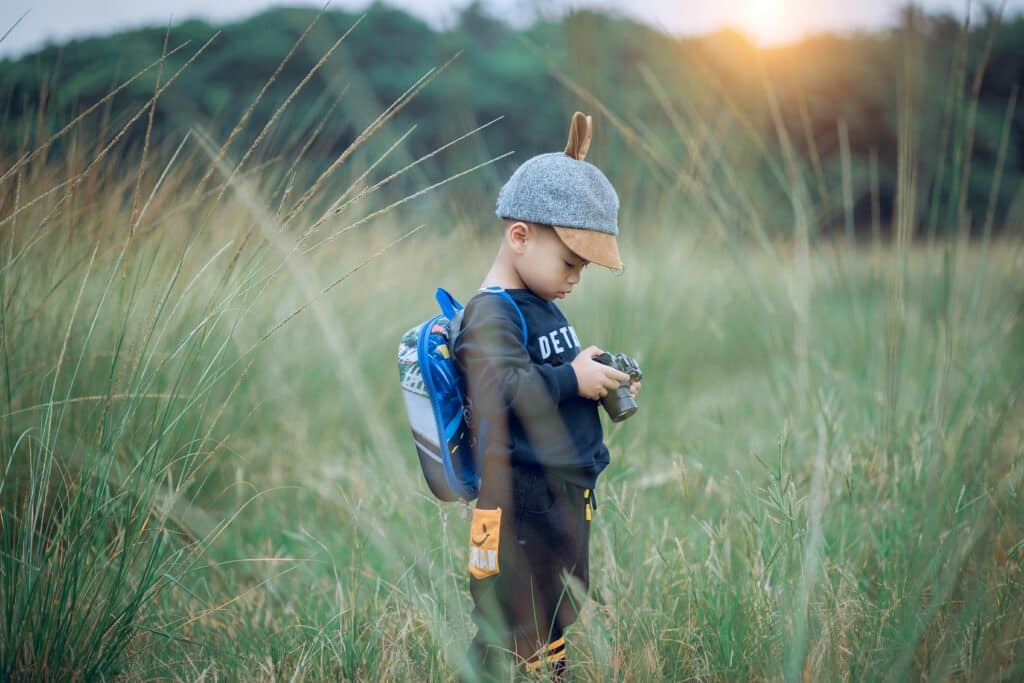 young boy in field with hat backpack and camera